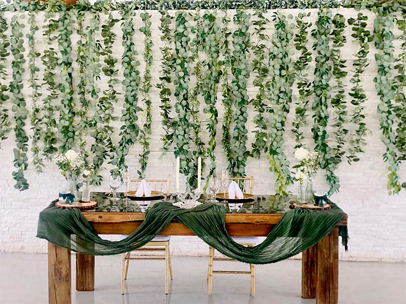 wooden table with green linen hanging on it and glasses and plates ontop with a brick wall covered in vines